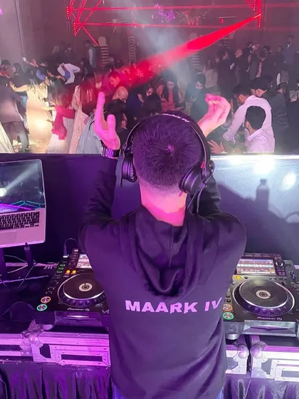 A view from my perspective, looking out at a packed dance floor during a wedding reception. My custom hoodie with 'MAARK IV' on the back is part of my brand, even when I'm focused on the mix.