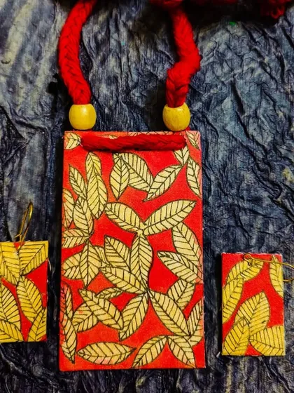 A beautiful shot of the red and yellow leaf-patterned fabric necklace set. The rich colors and detailed painting make this a warm, nature-inspired accessory.