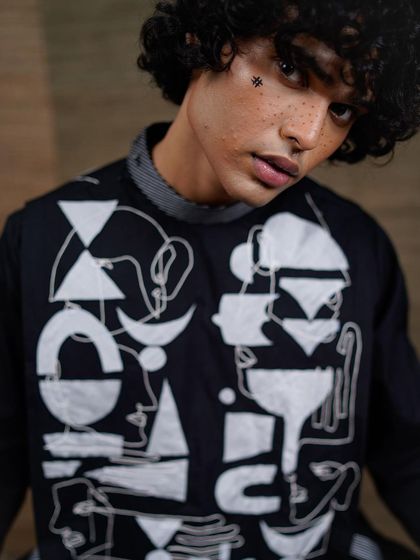 A close-up that reveals the intricate, abstract face-art on the garment and the subtle makeup on the model. This shot highlights the conceptual nature of the fashion collection.