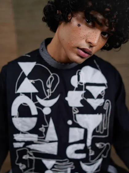 A close-up portrait focusing on the artistic details of the garment and the unique makeup. The abstract patterns on the clothing are mirrored in the small hash symbol drawn on the model's face.