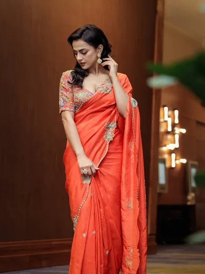 Shraddha Srinath looks radiant in this vibrant orange saree with a colorful embroidered blouse. This is a perfect look for promotions or a festive daytime event.