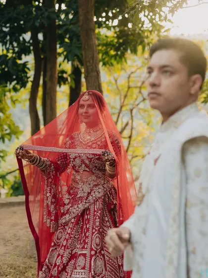 A romantic shot of the bride under her veil, with the groom approaching, set against the natural beauty of the outdoors.