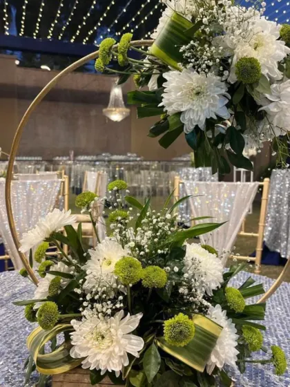 This unique centerpiece features a golden hoop adorned with white chrysanthemums and baby's breath, adding a contemporary touch to the sangeet decor.
