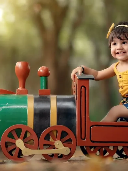 A big, happy smile from the train conductor. This little girl is having a wonderful time during her outdoor train-themed photoshoot.