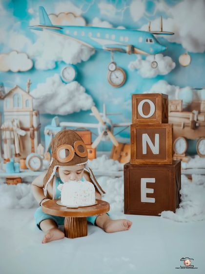 A little pilot takes a break from flying to enjoy his first birthday cake. The vintage aviator hat and the cloudy sky backdrop make this a truly special themed shoot.