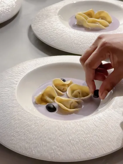 A chef carefully plating tortellini in a lavender-colored sauce. This dish was part of a menu where each course was designed to reflect the balance and form of the art at Galerie Isa.