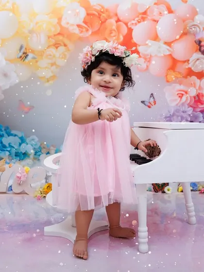 A little girl in a pink dress stands by a miniature piano in a dreamy, butterfly-filled setting for her first birthday.