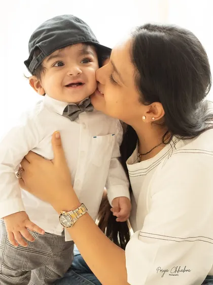 You are my sunshine. A mother gives her son a sweet kiss on the cheek during his one-year-old milestone photoshoot, complete with a cute cap and bow tie.