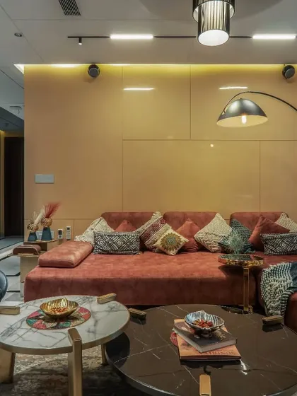 This cozy family lounge uses a warm color palette with a terracotta-colored sofa and patterned cushions. An elegant arc floor lamp provides focused lighting, while marble-topped coffee tables add a touch of luxury.