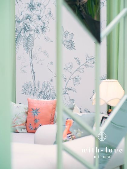 A peek through the sage green structure of 'The Conservatory', revealing the custom botanical wallpaper and colorful accent pillows inside.