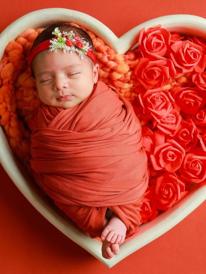 A slightly wider angle of the red rose heart setup, showing the baby's full swaddle and peaceful expression.