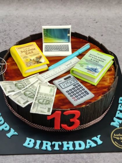 An office-themed cake for a Chartered Accountant. This cake is topped with an edible laptop, calculator, accounting books, and even edible Indian currency notes.