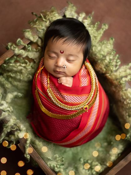 A tight close-up of the baby's face, wrapped snugly in the red saree. This shot is all about capturing the pure innocence of the newborn.
