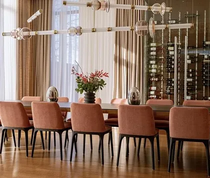 This view shows the Luna Kaleido fixture spanning the length of a long dining table, with a wine cellar in the background. It's a perfect example of lighting designed for luxurious entertaining.