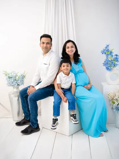 A complete family portrait, awaiting a new arrival. The simple, bright white studio setting allows the family's connection and the mother's radiant glow to be the focus.