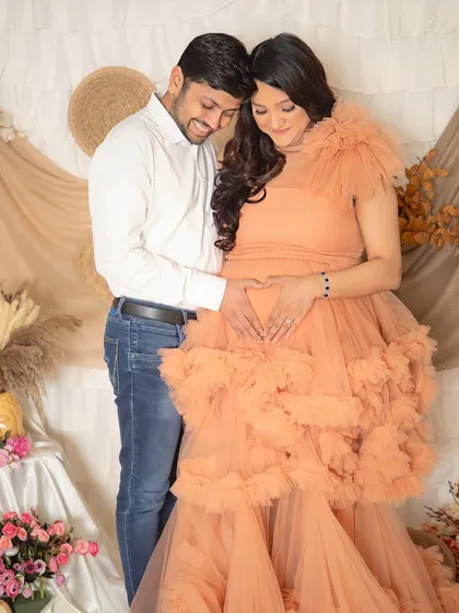 A loving embrace celebrating their journey together. The dad-to-be makes a heart shape with his hands on the baby bump, a simple and beautiful expression of love.
