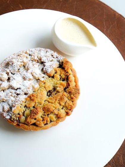 A delicious apple crumble tart, with a buttery crust and a sweet, spiced apple filling. It's served with a side of crème anglaise for extra indulgence.