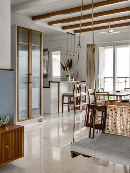 A wider view of the 'Malhar' living and dining space, showing the custom swing, full-height crockery unit, and a breakfast counter. Exposed ceiling rafters lend a charming cottage feel.
