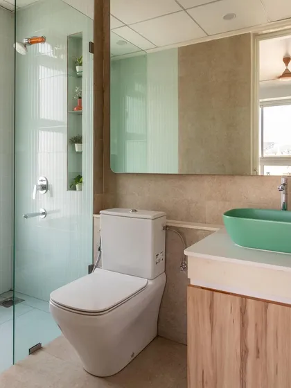 This bathroom combines soft blue tiles with earthy beige walls and a pop of color from the green vessel sink, creating a fresh and modern look.