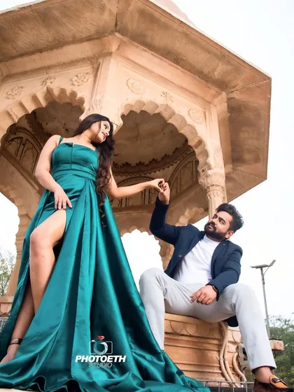 A dramatic and stylish pre-wedding shot against a stone gazebo. The bride's high-slit gown and the couple's pose create a confident and fashionable look.