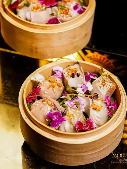 A close-up of our artfully crafted dim sum, garnished with edible flowers. Each piece is a delicate parcel of flavor, steamed to perfection and presented beautifully in traditional bamboo baskets, making them a highlight of our Pan-Asian menu.
