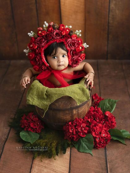 Seven-month-old Monishka in a beautiful red floral bonnet. The sitter stage is perfect for creative and colorful setups that showcase your baby's charm.