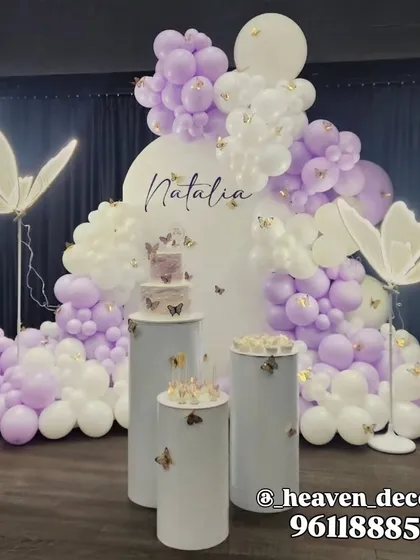A whimsical butterfly-themed birthday party setup. We used a cascade of lavender and white balloons, illuminated butterfly props, and custom pedestals for the cake, creating an enchanting atmosphere for the celebration.