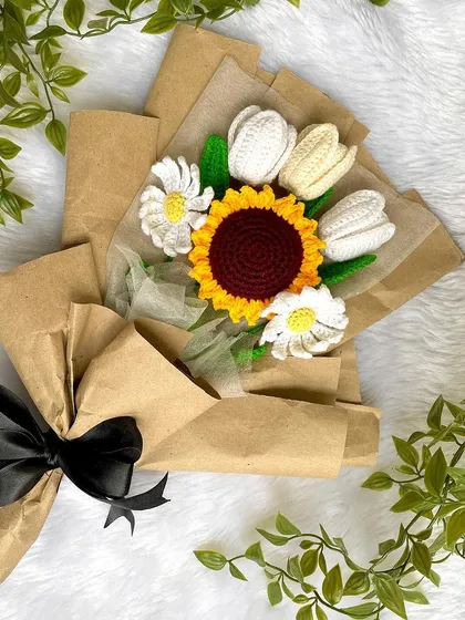 The beautiful tulip, sunflower, and daisy bouquet resting on a white background, tied with a simple black ribbon.