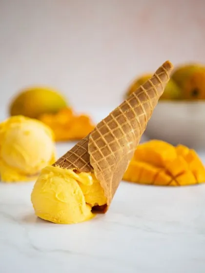 An overturned ice cream cone creates a sense of playful mishap. The vibrant mango color pops against the clean marble background, making for a simple yet effective summer-themed shot.