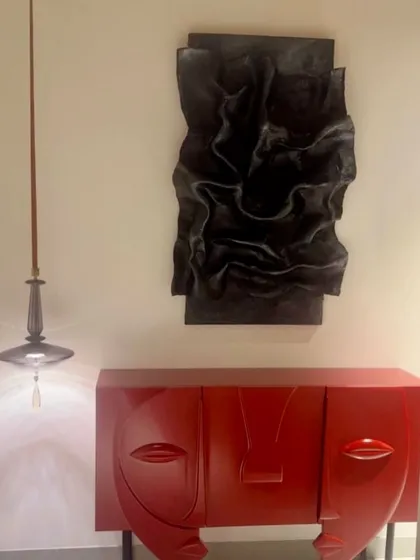 A dramatic black sculptural piece installed above a vibrant red console in a Kanpur residence. The contrast in color and form makes for a bold and artistic entryway statement.