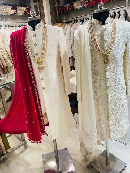 Two of my popular ivory sherwani sets on display. One is paired with a bright red stole and the other with a matching white one, showing how a simple change of accessory can create a different look. Both come with matching groom necklaces.