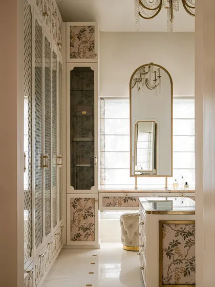 A different angle of the walk-in closet, showing the arched vanity mirror with brass trim and a plush tufted ottoman, creating a refined and glamorous dressing area.