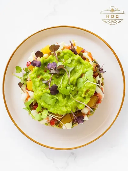This beautifully constructed avocado tartare is layered with finely diced vegetables and pomegranate seeds, then topped with fresh guacamole and microgreens. It is a refreshing and visually stunning dish.
