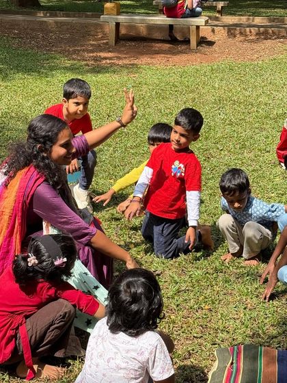 An interactive moment where I'm playing a game with the children, sitting on the grass. These games help build community and get everyone moving and laughing.