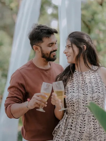 A celebratory toast to their future together. This shot captures a simple, happy moment during a relaxed outdoor pre-wedding session, framed by soft white drapes.