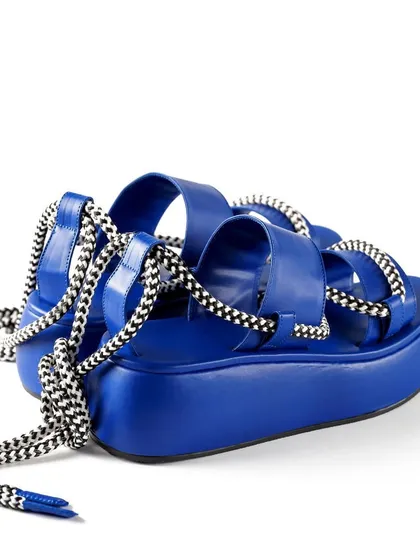 A dynamic three-quarter view of the blue platform sandals, showing off their height and the intricate lacing of the straps.