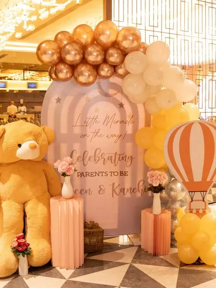 The personalized welcome stand for the 'Little Miracle' baby shower, featuring a giant teddy bear, a hot air balloon cutout, and a warm color palette of peach and gold.