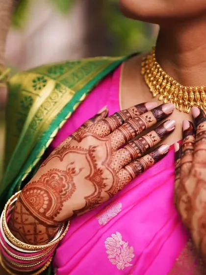 A professionally shot photo of a bride's henna stain. The deep color of the mehendi beautifully complements her traditional pink saree and gold jewelry.