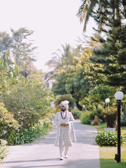 A full-length shot of the groom walking through a beautiful garden path, looking confident and ready for his big day.