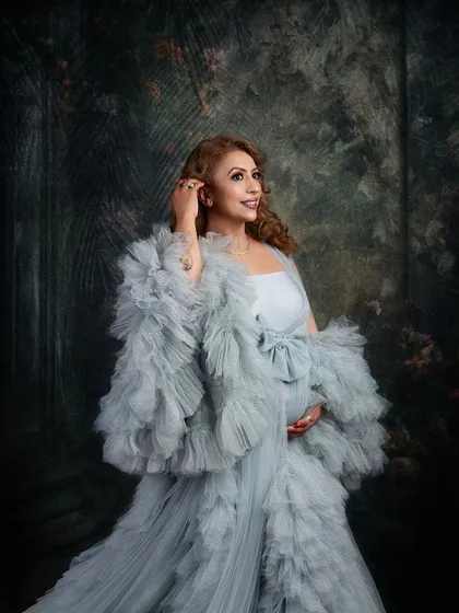 A beautiful close-up in a stunning grey ruffled gown. The painterly background and soft lighting create a sophisticated and elegant mood for this maternity portrait.