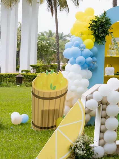 A detail shot of the lemonade party decor, featuring a large lemon slice prop, a barrel of lemons, and a blue, yellow, and white balloon garland.
