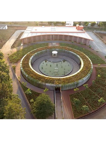 This aerial shot captures the unique spiral form of the memorial complex, with its central water body and surrounding green roof. The design was intended to create a landmark that feels both significant and deeply rooted in the earth.