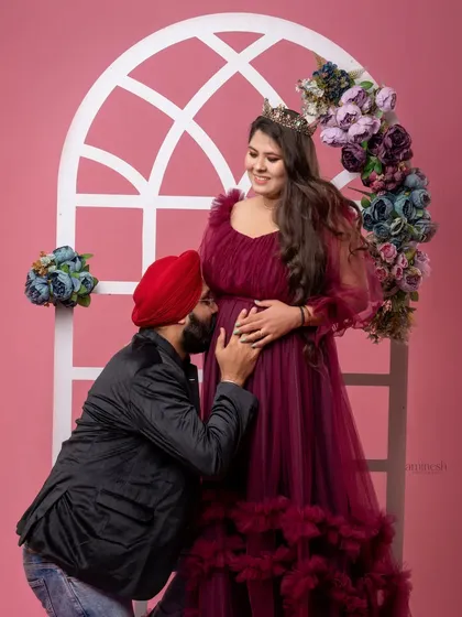 This studio shot combines a beautiful gown with an intimate moment. The partner's gentle kiss on the baby bump is a classic expression of love and anticipation.