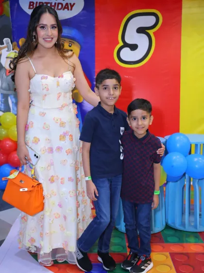 A mother and her two sons celebrate a 5th birthday with a Lego-themed backdrop. The bright, blocky design is perfect for a young builder.