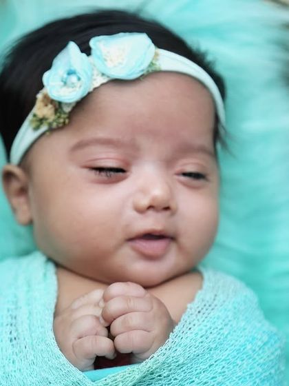 A close-up of a sleeping twin girl, swaddled in a beautiful turquoise wrap. Her peaceful expression is just precious.