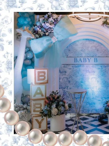 A close-up of the Dior-inspired photo booth, featuring a large blue bow, 'BABY' blocks, and a giraffe prop, all framed with a pearl border effect for extra elegance.