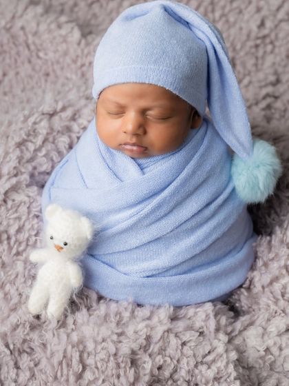 A simple and sweet portrait focusing on the baby's peaceful expression. The light blue wrap and matching pom-pom hat create a soft, classic look.