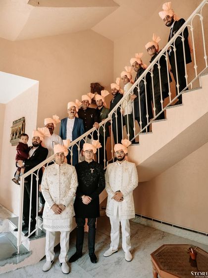 The groom's family and friends, all wearing traditional 'safas', pose on a staircase, a wonderful capture of family unity at a destination wedding.