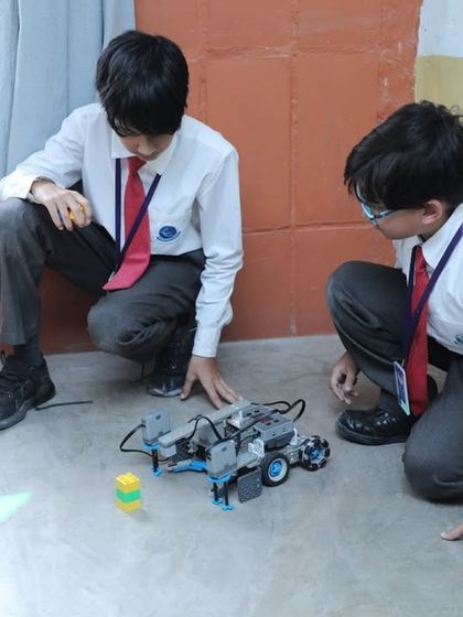 Two students test their robot on the floor, observing its movement and making adjustments. This iterative process of testing and refining is fundamental to engineering and robotics.