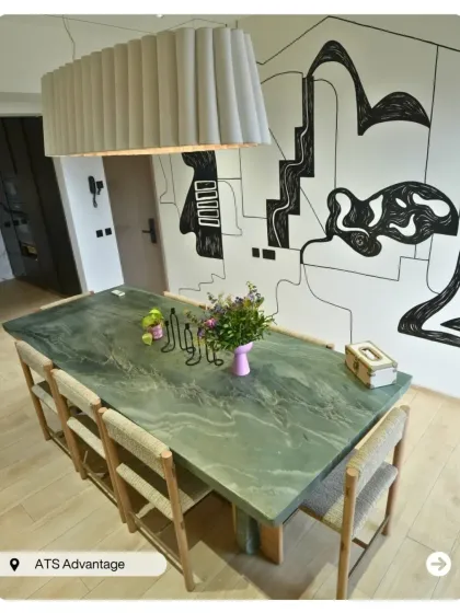 A unique dining area with a green stone tabletop and an abstract mural wall. The oversized fabric pendant light adds a soft, contemporary touch to this artistic space.